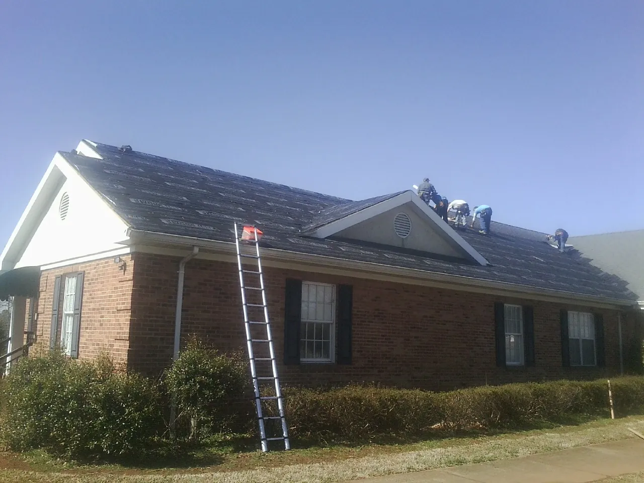 Crew tearing shingles off a brick ranch roof with a ladder set — Metal Roof Repair work by our crew in Corryton
