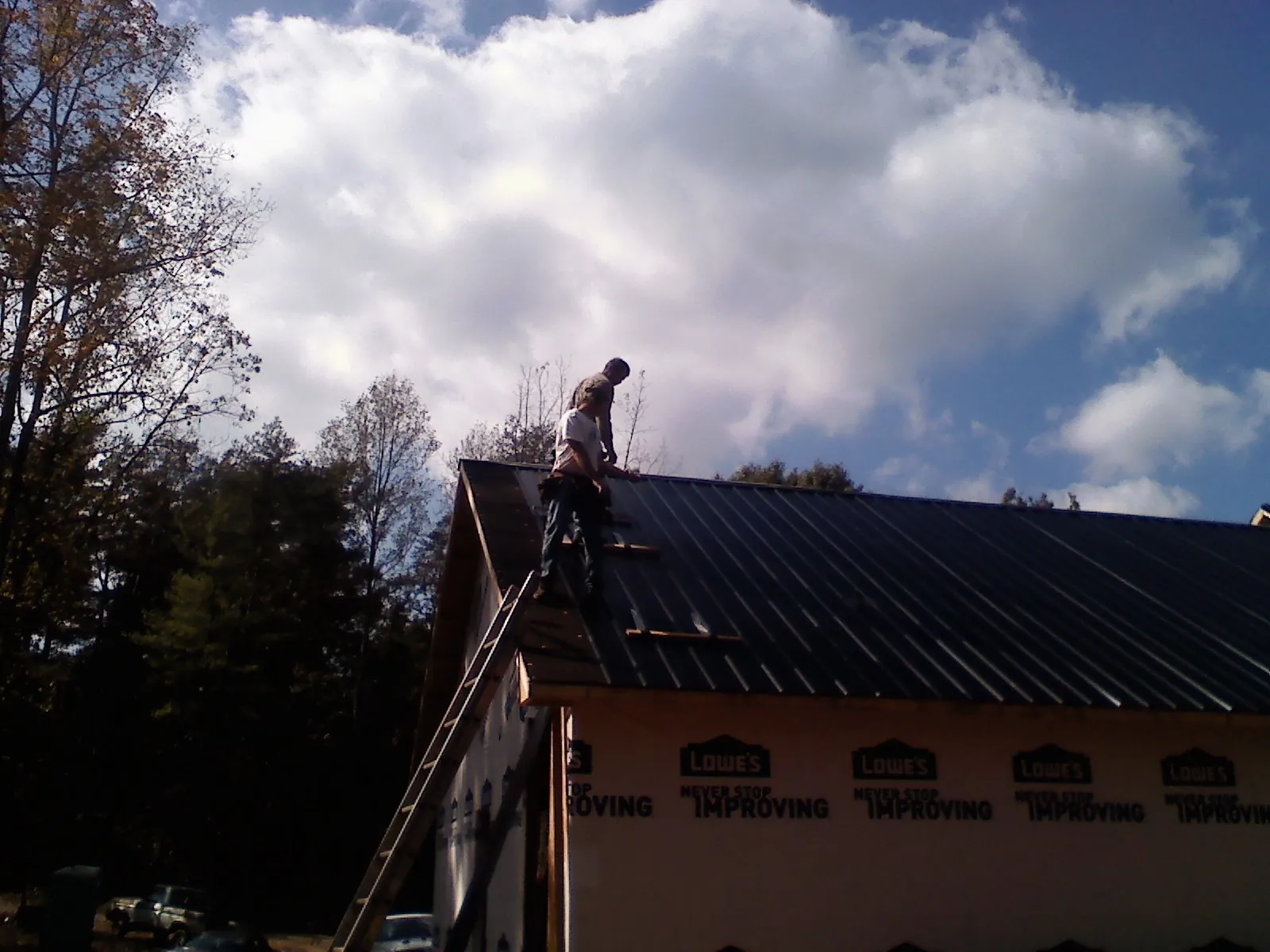 Roofer fastening dark metal panels high against a cloudy sky, from a Roof Inspection job in Corryton