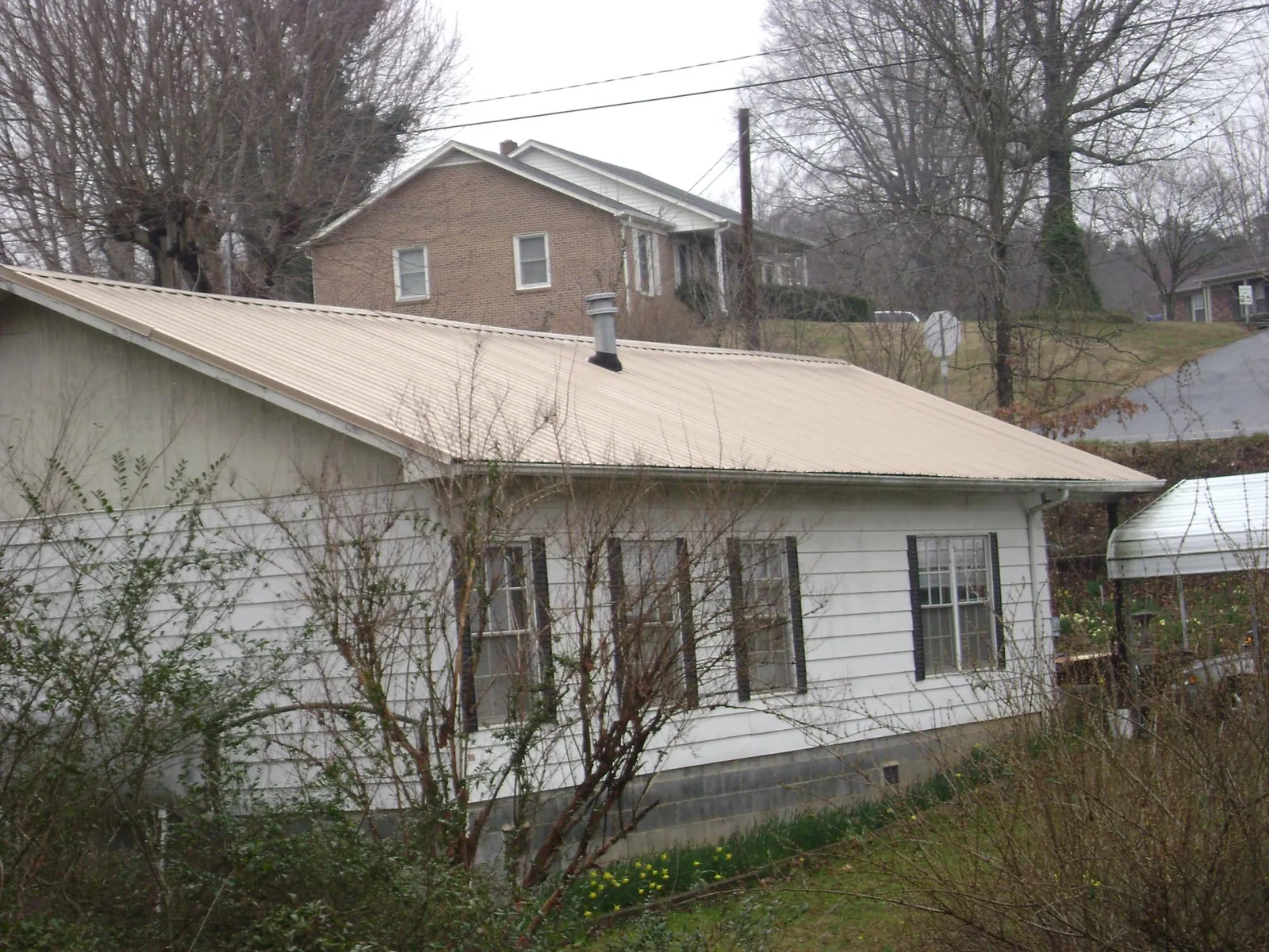 Tan metal roof on a white sided house set into a hillside — Commercial Roofing by Roofing Brothers in Corryton